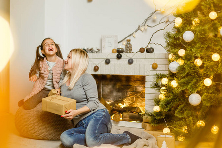 快乐的妈妈和可爱的女儿交换礼物，在客厅的圣诞树附近玩，圣诞快乐，节日快乐