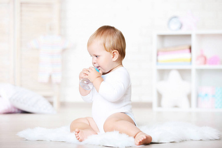 小男孩从瓶子里喝水，坐在家里的地毯上