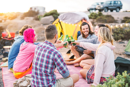 一群朋友在海滩上的烧烤晚宴上喝啤酒，快乐的人在帐篷里露营，在烧烤友谊和青年生活方式度假的概念上品尝啤酒瓶，玩得很开心