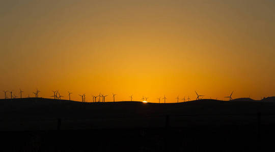 背景为日落的风力涡轮机视图