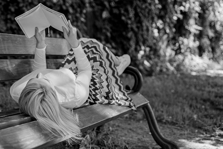 女孩卧椅休闲与书, 绿色自然背景。妇女花闲暇与书。有趣的书。聪明又漂亮女孩在户外看书, 同时在板凳上放松。聪明的女士放松