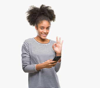 年轻的AFRO美国女性使用智能手机在孤立的背景下发短信，用手指做OK标志，优秀的符号