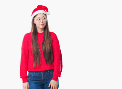 年轻的中国女人在孤立的背景上戴着圣诞帽，微笑着看着一边，凝视着远方的思考。