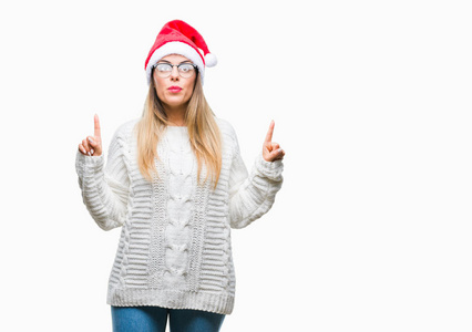 年轻漂亮的女人戴着圣诞帽在孤立的背景上惊讶和惊讶地抬头，用手指和举起的手臂指着。