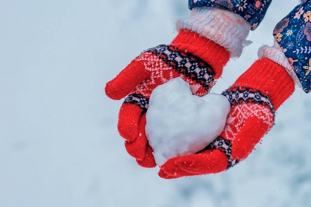 雪心在女孩手中。 双手穿着针织手套，捧着雪做的红心。