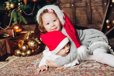 孩子们在装饰冷杉树的地毯上戴着圣诞老人的帽子