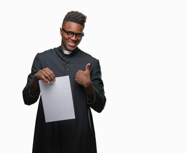 年轻的非洲裔美国牧师，在孤立的背景下，拿着白纸，开心地笑着，做着好的标志，用手指竖起大拇指，很好的标志