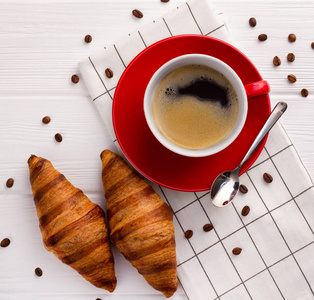羊角面包和一杯咖啡放在白色的木桌上。 欧式早餐从上面的视图平面拍摄。