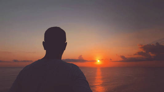 日落日出时间的人在海洋上的剪影。