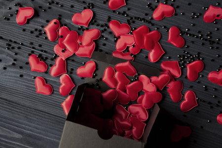 红色的心是从深蓝色的木桌上的一个黑色礼品盒里倒出来的。