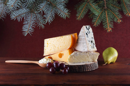 木制背景和圣诞树树枝上的奶酪品种。 瑞士奶酪DorbluCamembert和家庭干酪圣诞节。 乳制品柠檬葡萄和梨木板