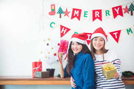 两个美丽的亚洲女孩拿着礼品盒，在家里的圣诞聚会上微笑。