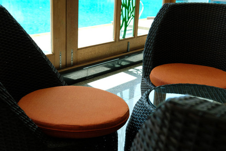舒适的藤椅，带有橙色的坐垫，在游泳池旁边的现代住宅客厅里