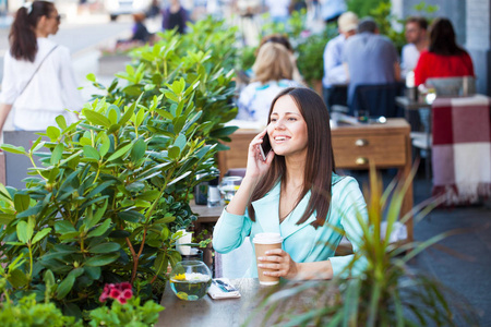 优雅的女孩，留着长长的黑发，在户外咖啡馆休息时给别人打电话，喝杯咖啡。严肃时尚女性的户外照片