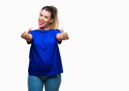年轻漂亮的女人穿着休闲的蓝色T恤，在孤立的背景上，批准用手竖起大拇指做积极的手势，微笑，为成功而高兴。 看着相机赢家的手势。