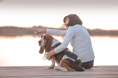 快乐的年轻女人和她的狗贝塞特猎犬坐在木墩上。 带小狗的女人。