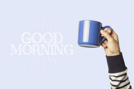 男性手拿着一个蓝色的杯子，上面有热咖啡或蓝色背景的茶。 添加文本早上好。 早餐概念与热咖啡。
