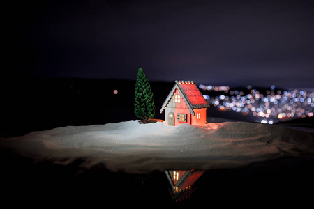 圣诞节和新年的微型房子在雪中与杉树。 雪地上的小玩具屋，背景上有树和博克城的灯。 圣诞装饰品。 假日概念。