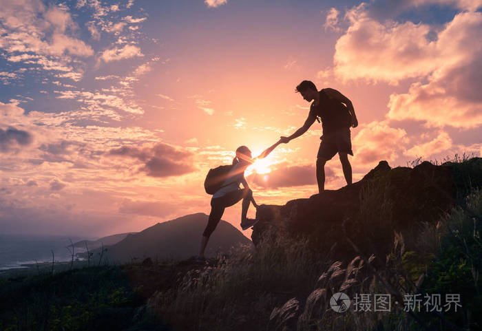 人们在日出时互相帮助爬山.