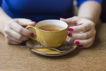 女孩拿着黄色的茶杯坐在木桌上，在咖啡馆里靠近