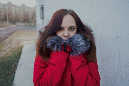 在阴天，穿着红色夹克的快乐美丽的年轻女孩在外面摆姿势。 学生的情感肖像。 街头风格
