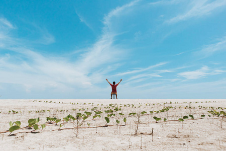 人站在白色的沙滩上，明亮的蓝天。 自由的概念。
