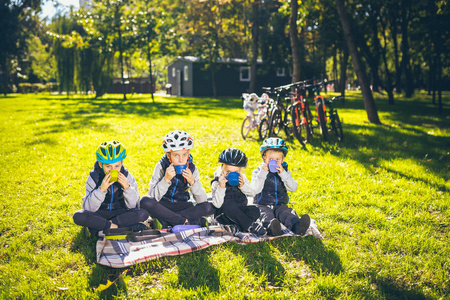 主题活跃家庭假日性质。 成群的人，小孩子，三个兄弟姐妹，坐在自行车旁，在公园的绿草草坪上休息，喝杯子和热水瓶茶。
