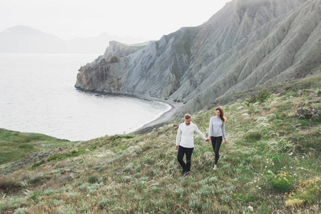 年轻夫妇走在北欧海岸，在春天的山景中，穿着休闲风格的衣服毛衣和牛仔裤。