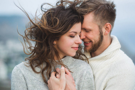 特写照片的夫妇与风在头发拥抱和快乐在一起。 两者都是毛衣