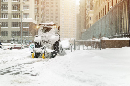 拖拉机用刷子和铲子清理城市街道上的雪，并在冬天大雪后停车。