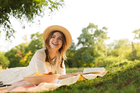 可爱的小女孩戴着夏帽在公园野餐，吃水果，看书