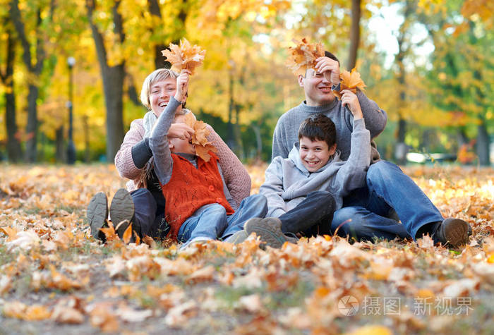 幸福的一家人坐在秋天的城市公园里落叶.