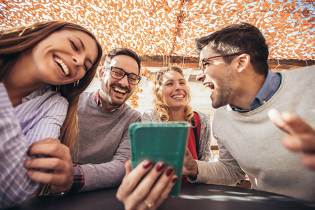一群四个朋友一起喝杯咖啡。 两个女人和两个男人在咖啡馆说笑和使用智能手机。