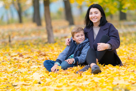 一对快乐微笑的母子坐在公园里黄色的落叶中。