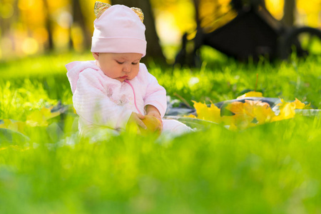 一个小女孩在公园里玩秋叶，她坐在郁郁葱葱的草地上，低角度地看着。