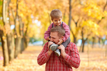 父子俩在秋天的城市公园玩和玩。 他们摆出微笑的姿势玩。 明亮的黄色树木。