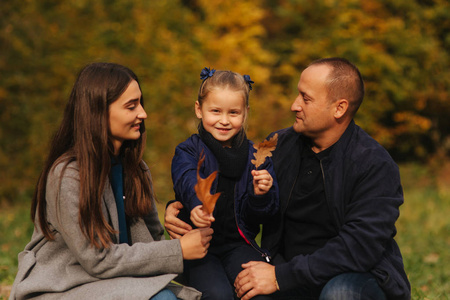 父亲和两个女儿在森林里。秋天的天气和五颜六色的背景。幸福的家庭。两个妹妹向爸爸示爱