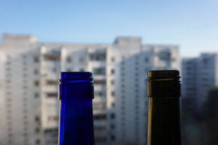 绿色和蓝色的葡萄酒和香槟半透明的瓶子靠在窗户上，有建筑物的背景。 家庭装饰阁楼背景。