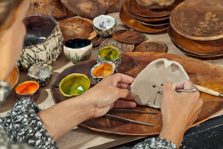 那个女孩在陶器碗上雕刻一件装饰品。 手工制品在家庭车间的桌子上。 有图纸和图案的陶瓷产品。