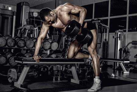 健美运动员在黑暗的健身房里用哑铃在背部最宽的肌肉上进行锻炼
