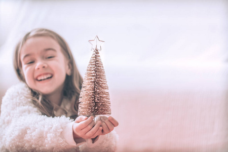 圣诞节背景与一个可爱的小女孩和一棵美丽的小树在一个女孩的手中，在一个轻背景。