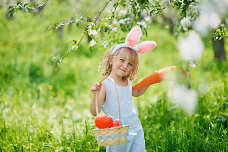 可爱的有趣女孩，在花园里有复活节彩蛋和兔子耳朵。 复活节的概念。 复活节猎蛋的笑孩子。 孩子在公园里，篮子里装满了鸡蛋，春天的概