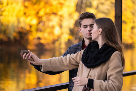那个人向那个女孩求婚。 一对年轻的相爱的夫妇站在秋天的公园里，有黄色的树。 一个男人拿着一个带戒指的盒子。 女人说不。