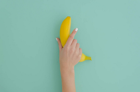 女性手拿着香蕉在薄荷蒂凡尼背景。最小的水果概念