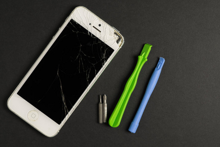 坏了的白色手机和修理工具包在黑暗的背景上