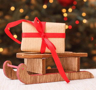 用彩带包装的圣诞礼物，放在木制雪橇上，圣诞树上放着背景灯