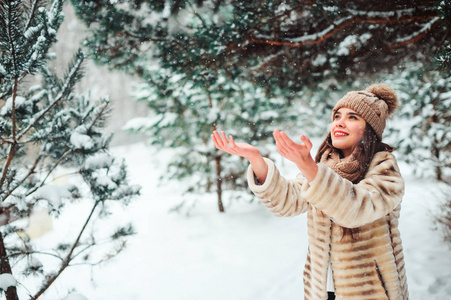快乐的女人在白雪皑皑的冬林里散步，在雪花上捕捉。 户外季节性活动的概念
