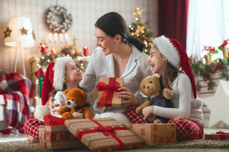 圣诞快乐，节日快乐 快乐的妈妈和她可爱的女儿交换礼物。 父母和小孩子在室内的树附近玩得很开心。 爱的家庭，房间里有礼物。图片