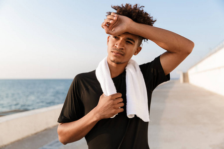 英俊的年轻人运动员站在海滩上用毛巾站在户外的形象。