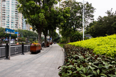 行人石走道钢黑色围栏旁边的道路。 有五颜六色花的大木花坛。 广州休闲公园步行道。